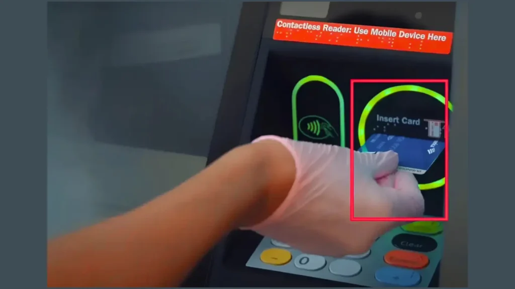 “Person wearing a glove inserting a bank card into an ATM machine slot marked ‘Insert Card’ with a contactless reader beside it.”
